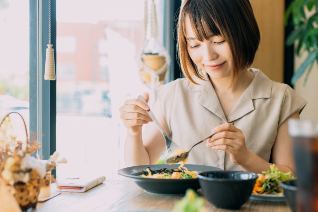 素敵なカフェでにこやかにスプーンとフォークでパスタをからめる主婦。