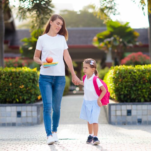 赤いカバンを背負って学校に登校する女の子とお母さんが手をつないでいます。